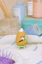 Close-up of a potato-shaped figurine sitting on a tiny green stool, amidst various beauty products.