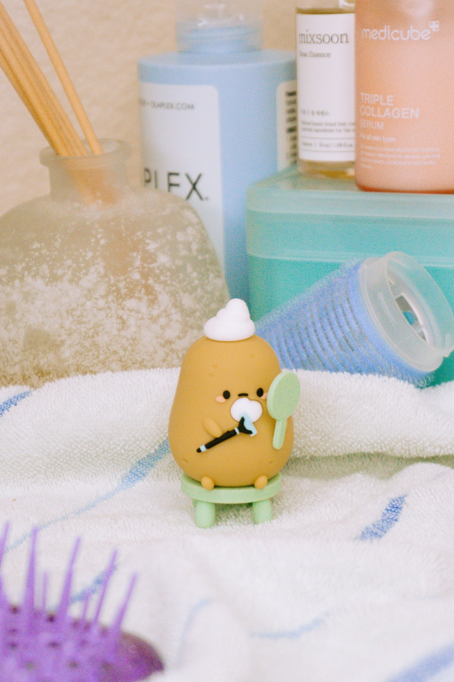 Close-up of a potato-shaped figurine sitting on a tiny green stool, amidst various beauty products.