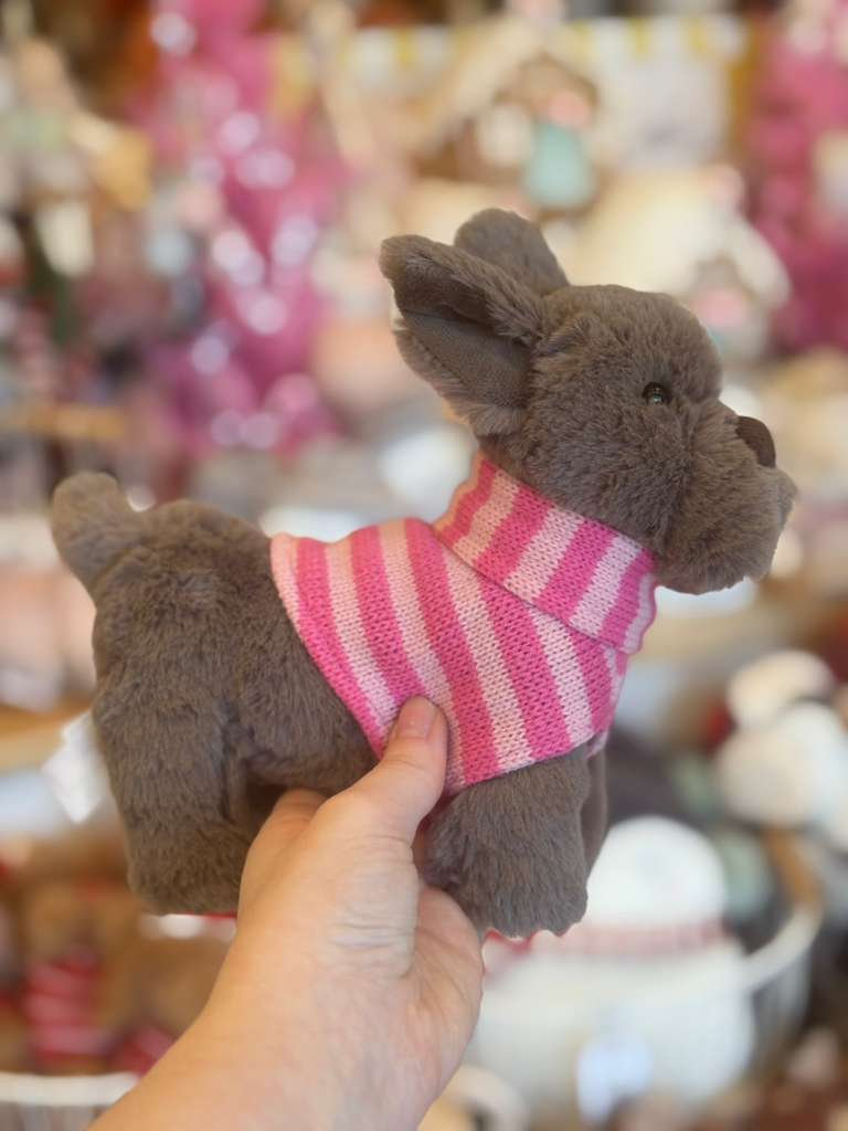 Plush toy donkey wearing a pink and white striped sweater held by a hand against a blurred background.