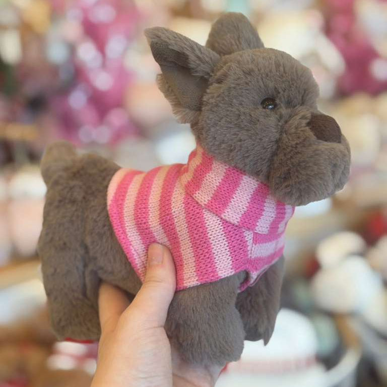 Plush dog toy wearing a pink sweater held by a hand with a blurred background