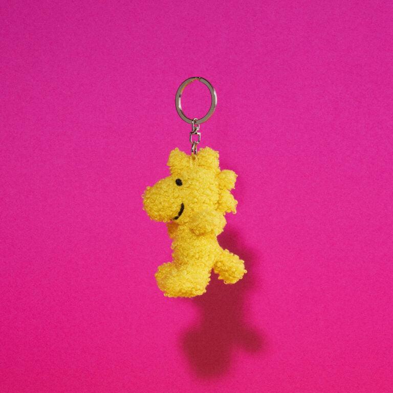 Yellow, plush Woodstock keychain on pink background.