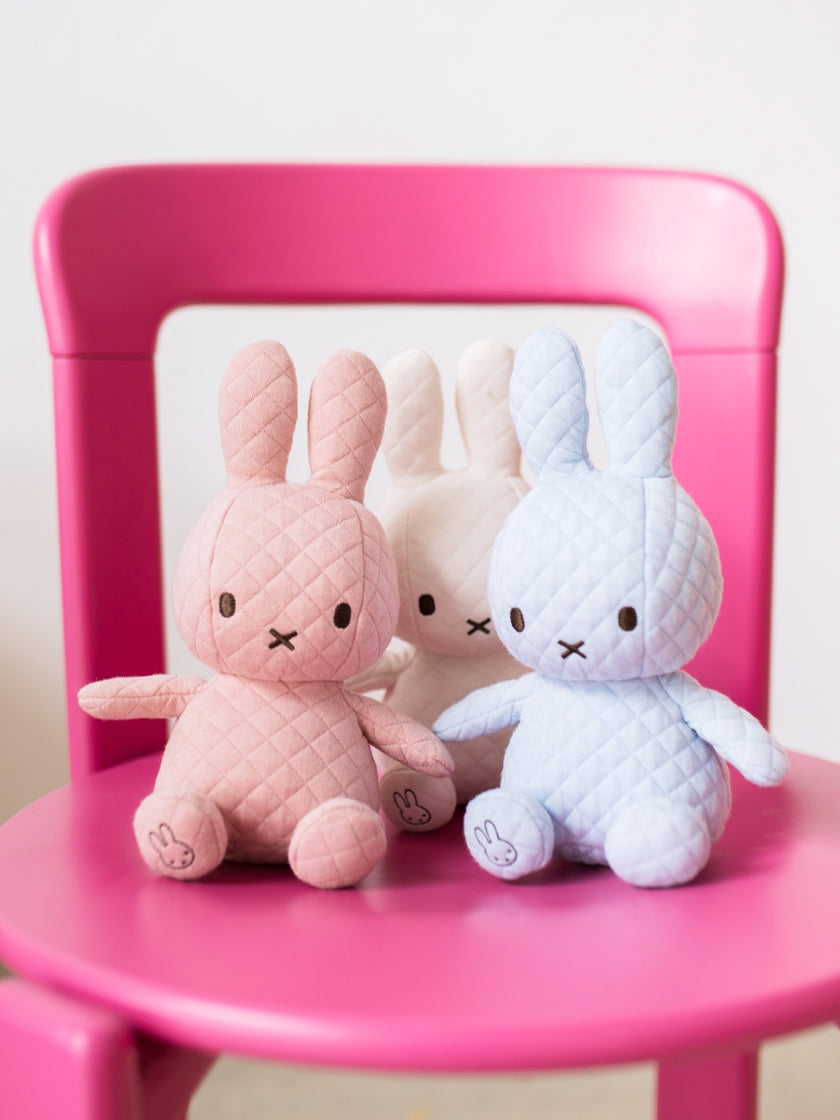 Three pastel bunny plush toys on a pink chair.