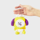 Hand holding a yellow and purple plush keychain with a white face.