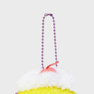 Close-up of a plush dessert keychain with a pink beaded chain, white frosting, and yellow base.
