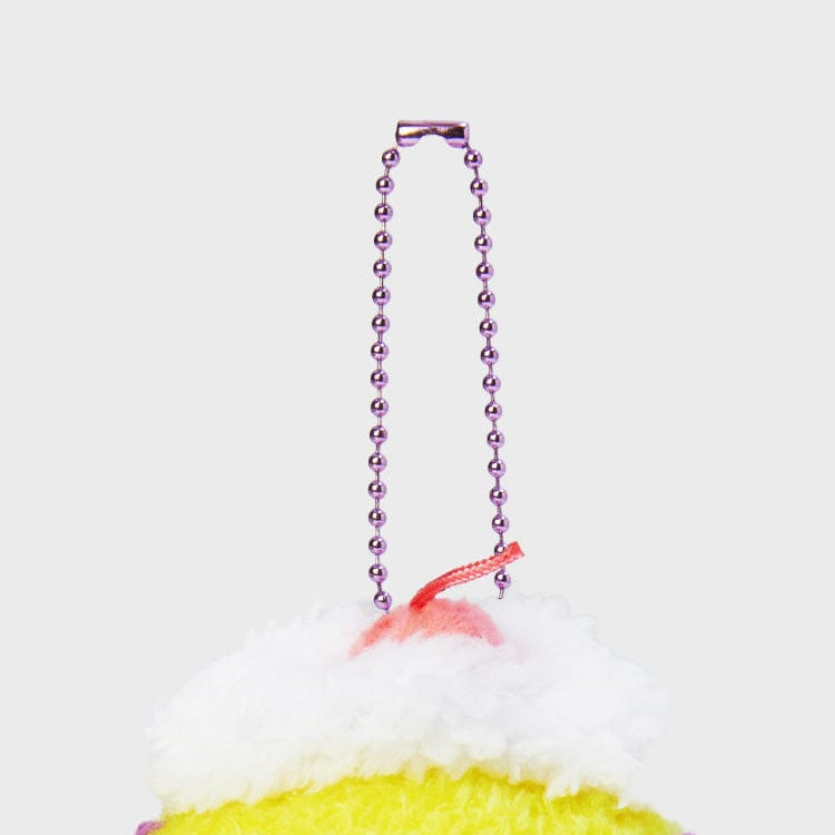 Close-up of a plush dessert keychain with a pink beaded chain, white frosting, and yellow base.