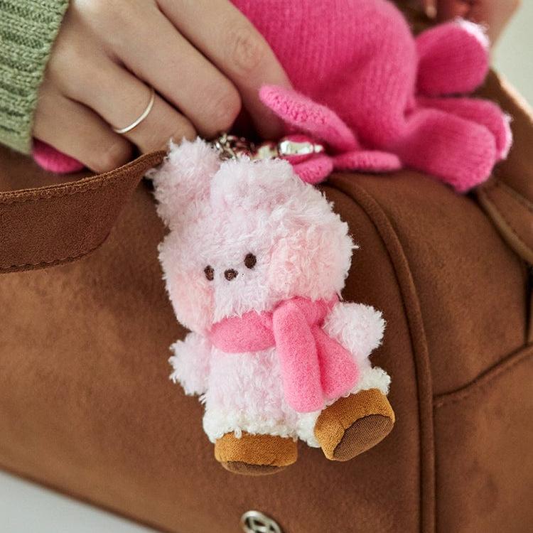 Pink and white plush bunny keychain with scarf hanging from a brown bag.