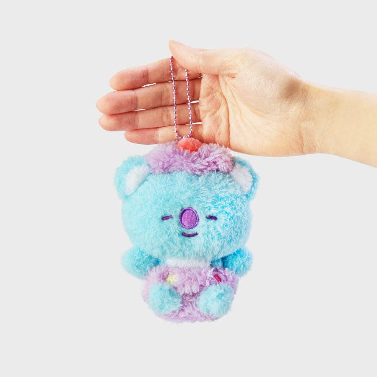 A hand holds a small, blue and lavender plush bear with a cherry on top, attached to a silver ball chain.