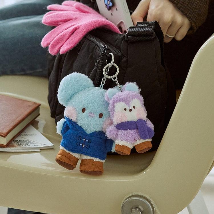 Two small plush keychains of cartoon animals wearing clothes attached to a black bag on a chair.