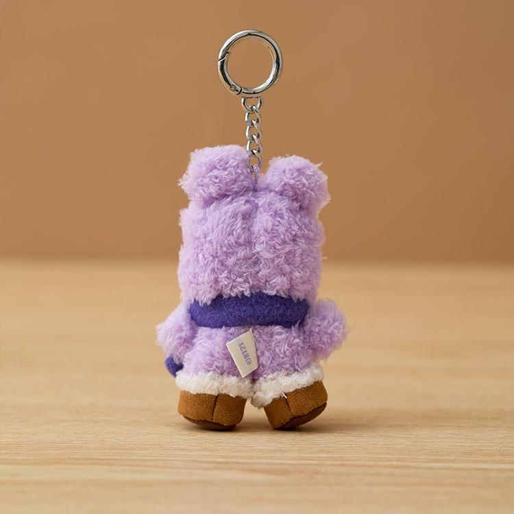 Back view of a purple plush keychain toy with brown feet, a white trim, and a dark purple scarf.