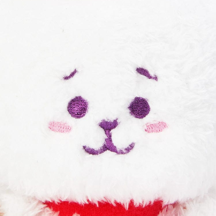 Close-up of a fluffy white plush toy with purple embroidered eyes, mouth, and eyebrows, and pink embroidered cheeks.