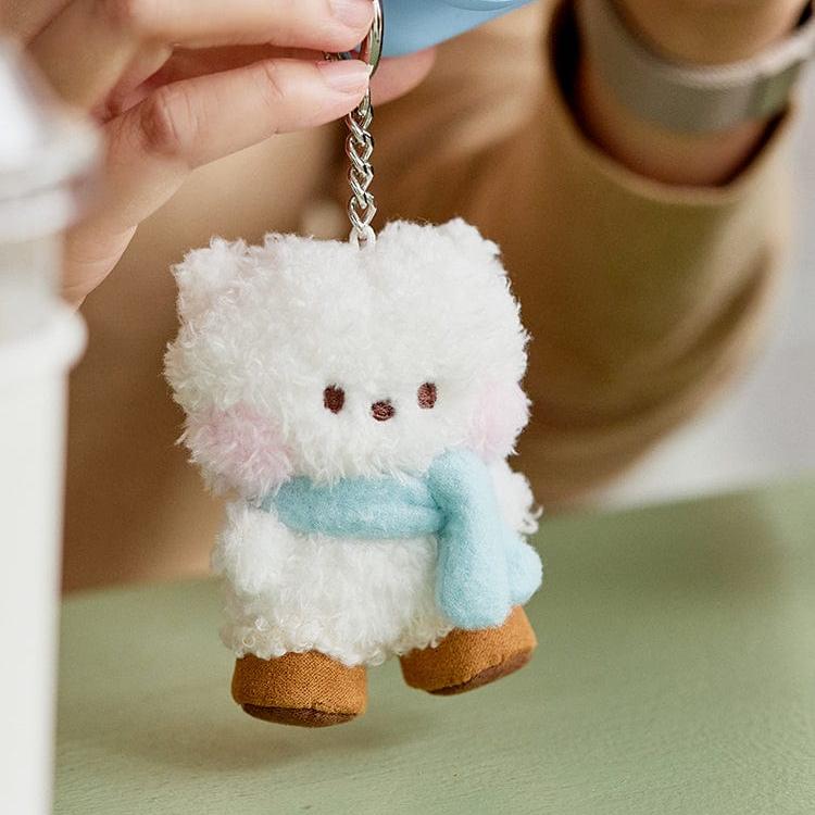 Close-up of a white, fuzzy bear keychain with a light blue scarf and brown shoes.