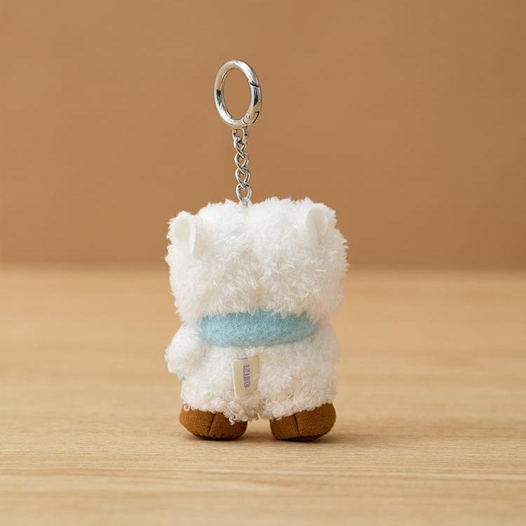 Rear view of white bear plushie wearing light blue scarf, hanging from metal keychain, standing on wooden surface.