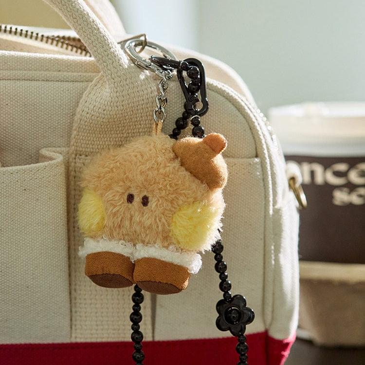 Close-up of a beige plush keychain hanging from a cream-colored canvas bag.
