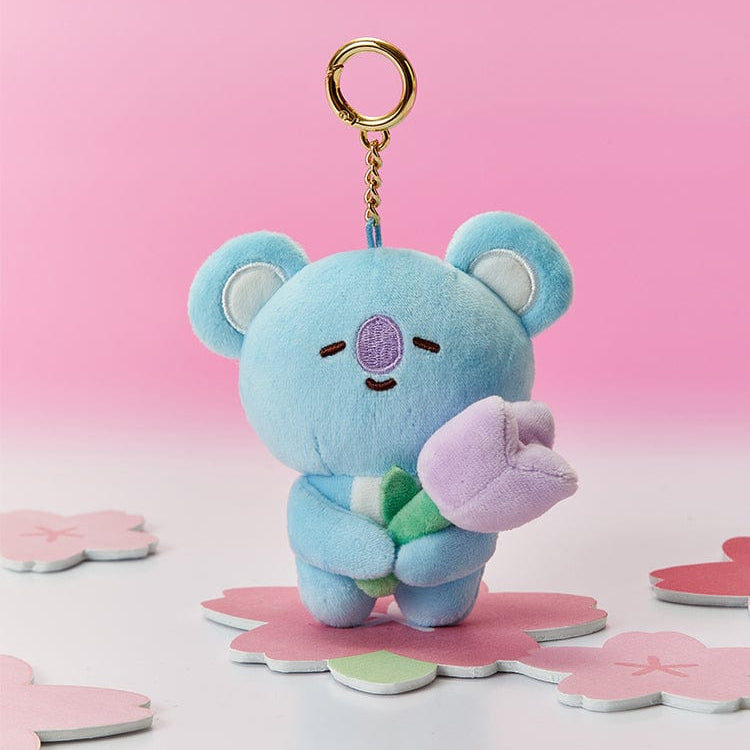 Blue plush koala bear keychain holding a purple tulip on a pink flower platform.