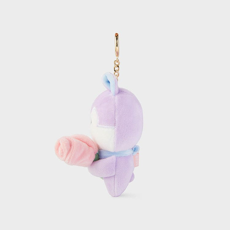 Side view of a lavender plush rabbit holding a pink rose. The plush rabbit has a blue ribbon around its neck and a golden chain attached to its head. The background is a solid light gray.