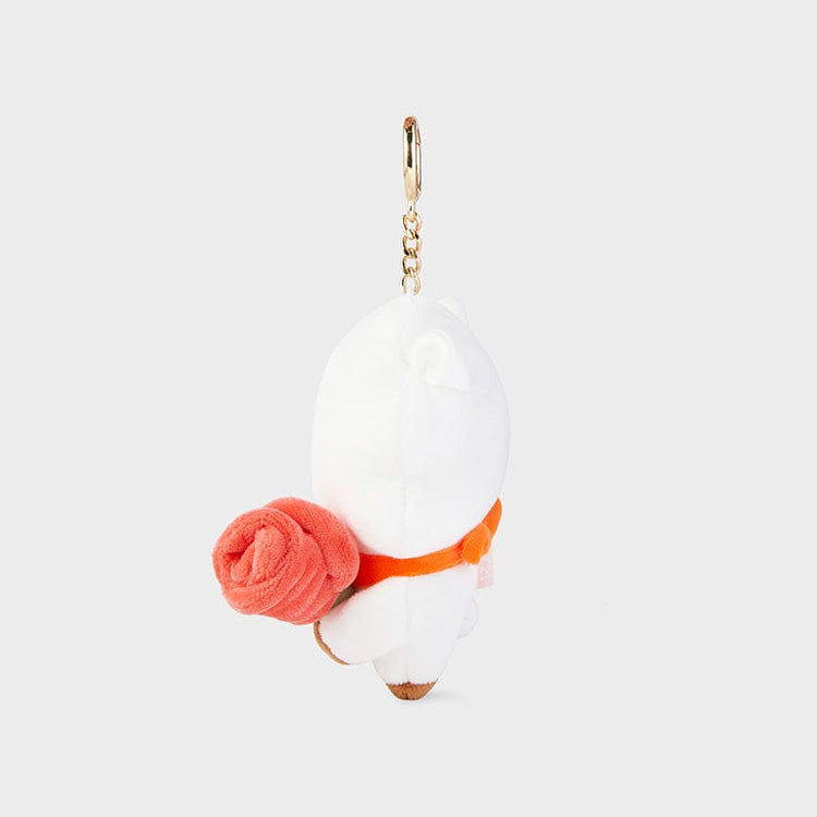 A small, white, plush keychain of a bear with an orange necktie, holding a red rose.