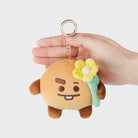 A plush keychain of a cartoon character holding a yellow flower, being held in a hand.