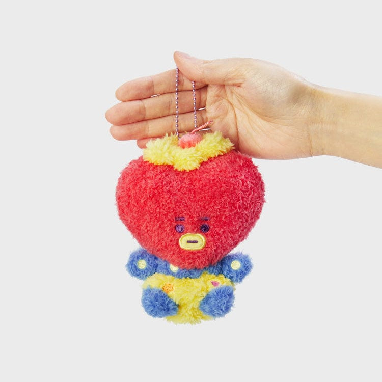 Hand holding a plush toy of a red heart-shaped character with a yellow ruff, blue and yellow body, and a chain.
