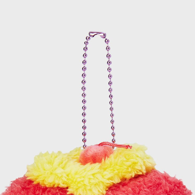 Close-up of a keychain with a metallic purple beaded chain and a fluffy red and yellow plush charm with a pink pom-pom.