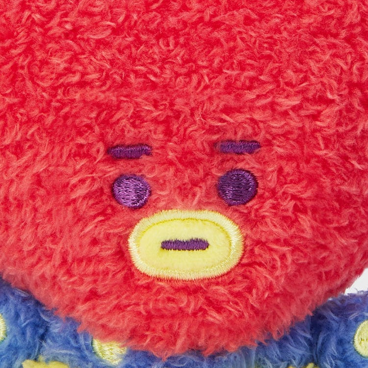 Close-up of a red plush toy with a blue and yellow polka dot outfit, featuring purple eyes and a yellow outlined mouth.