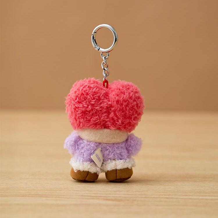 Back of a plush keyring featuring a heart-shaped head, a lavender shirt with a white hem, and brown shoes.