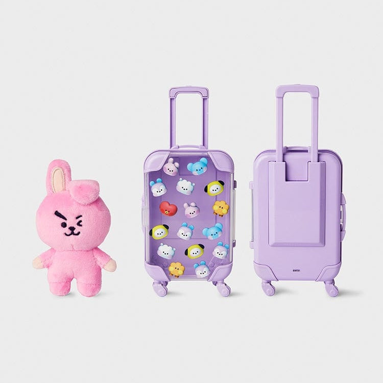 Pink bunny plush next to two small purple suitcases, one clear and full of charms.