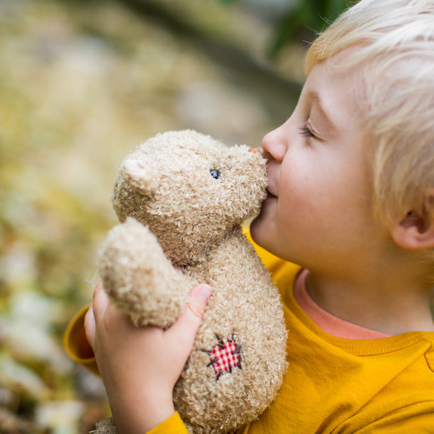 Child kissing a teddy bear outdoors
