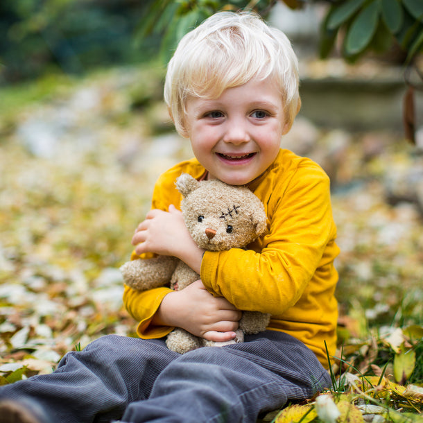 Child in a yellow jacket holding a teddy bear outdoors with blurred background