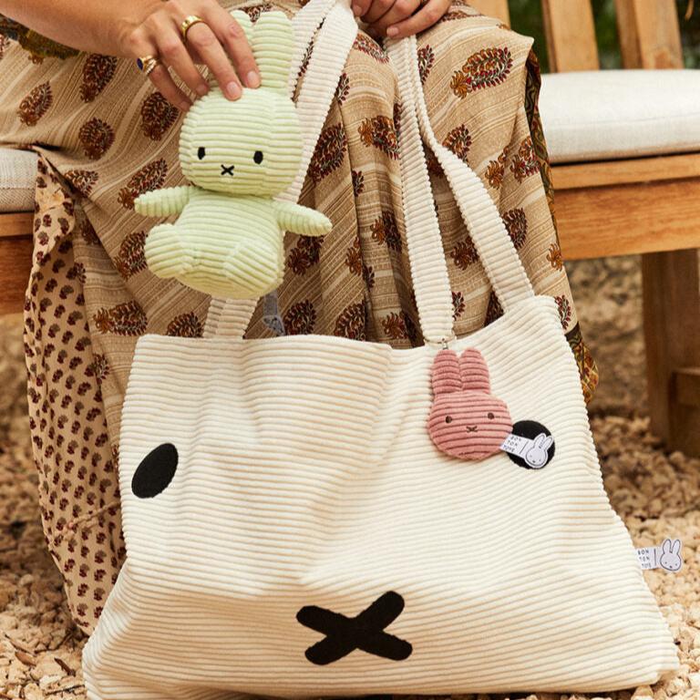 Person holding a green bunny doll and a white corduroy tote bag with bunny decorations.
