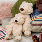Two cream teddy bears on an assortment of colorful pillows and fuzzy blankets.