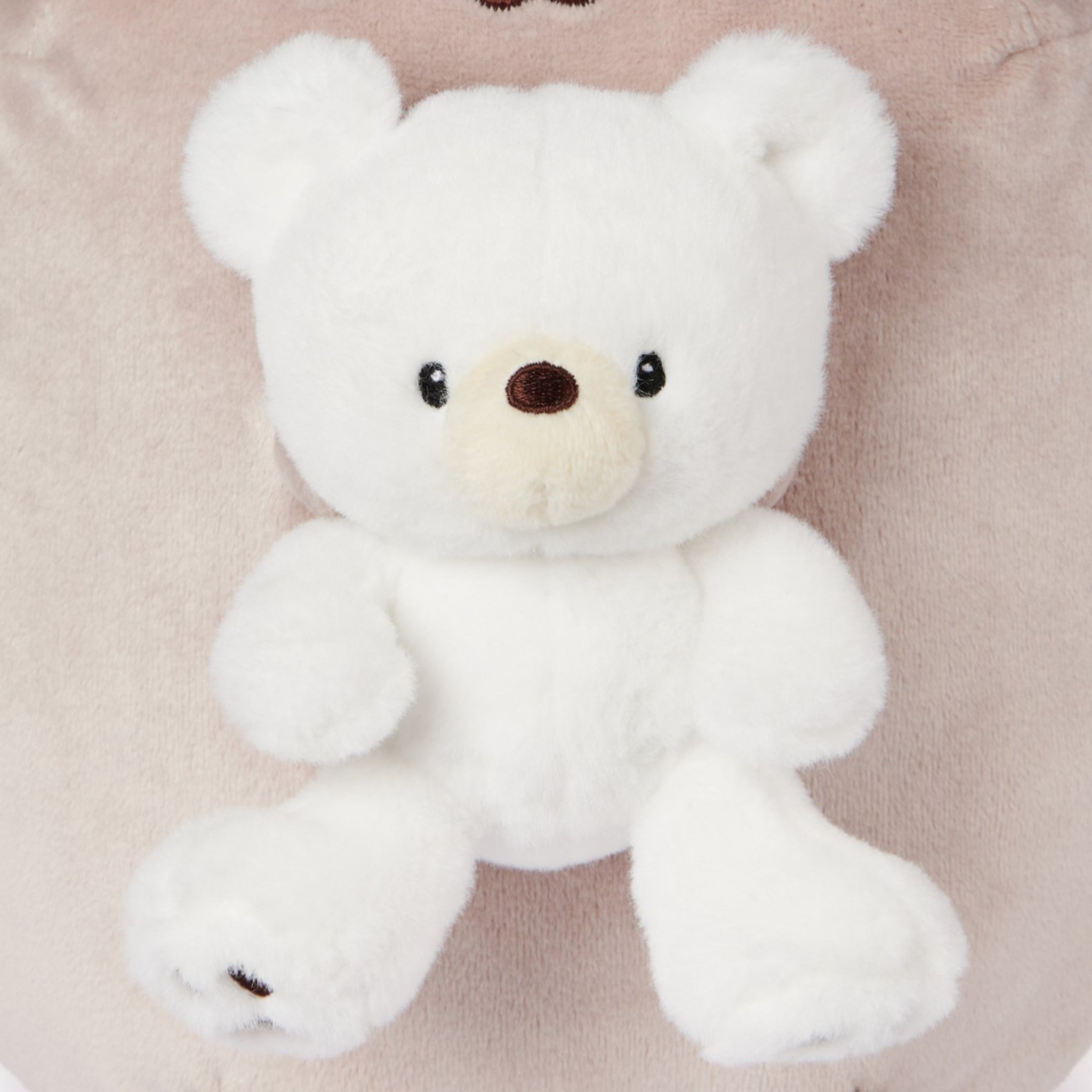 White teddy bear on a beige plush cushion.