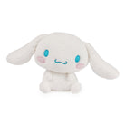White Cinnamoroll plush toy with blue eyes and mouth, and pink cheeks, seated on a white background.