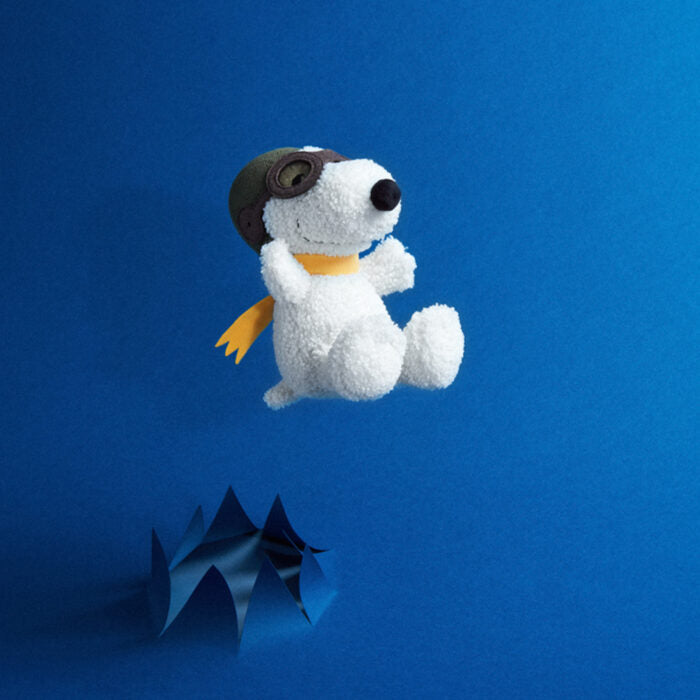 Stuffed Snoopy in pilot gear, flying over a blue paper cut-out.