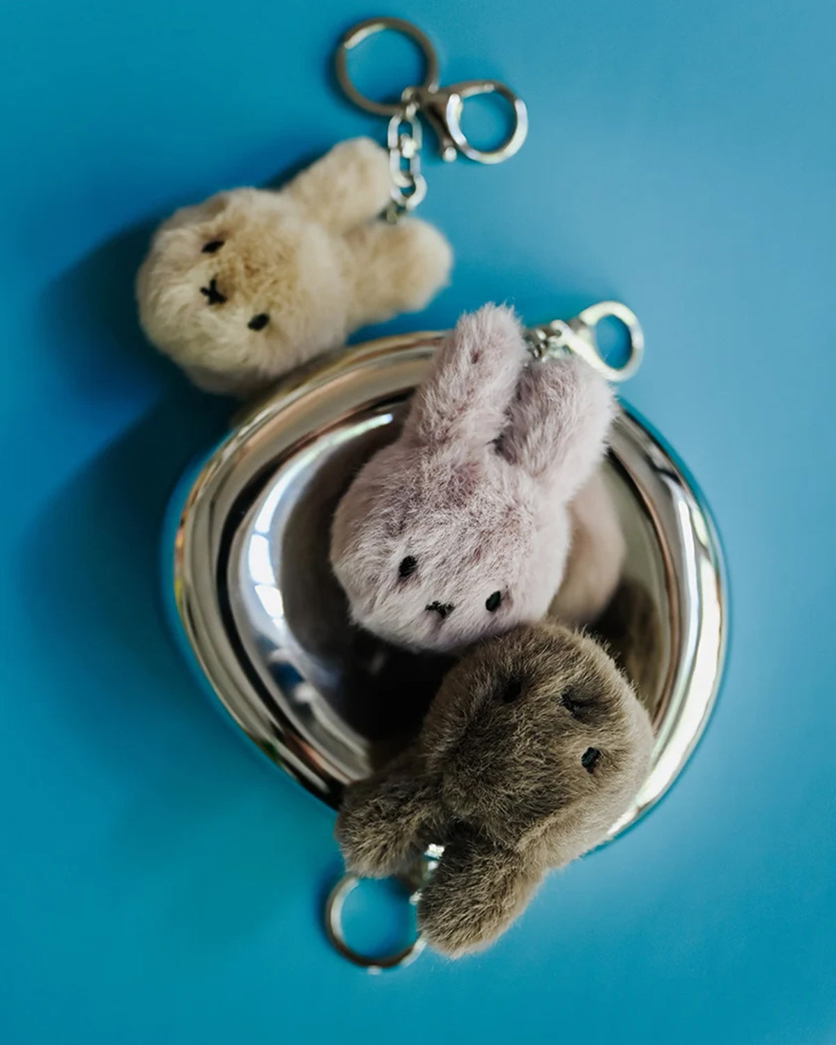 Three bunny-shaped fuzzy keychains in a silver dish on a blue background.