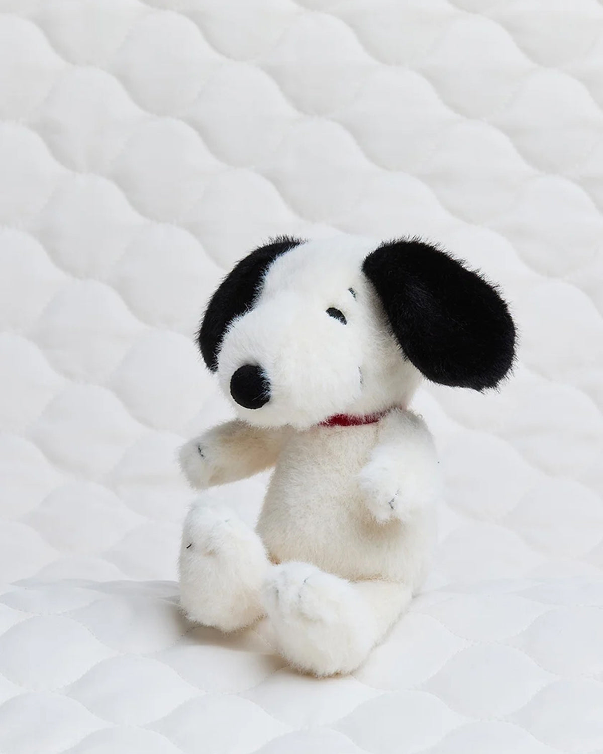 Stuffed Snoopy dog sitting on white quilted surface.