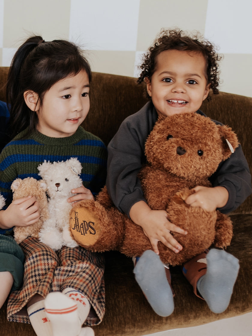 Two young children holding teddy bears while sitting on a couch.