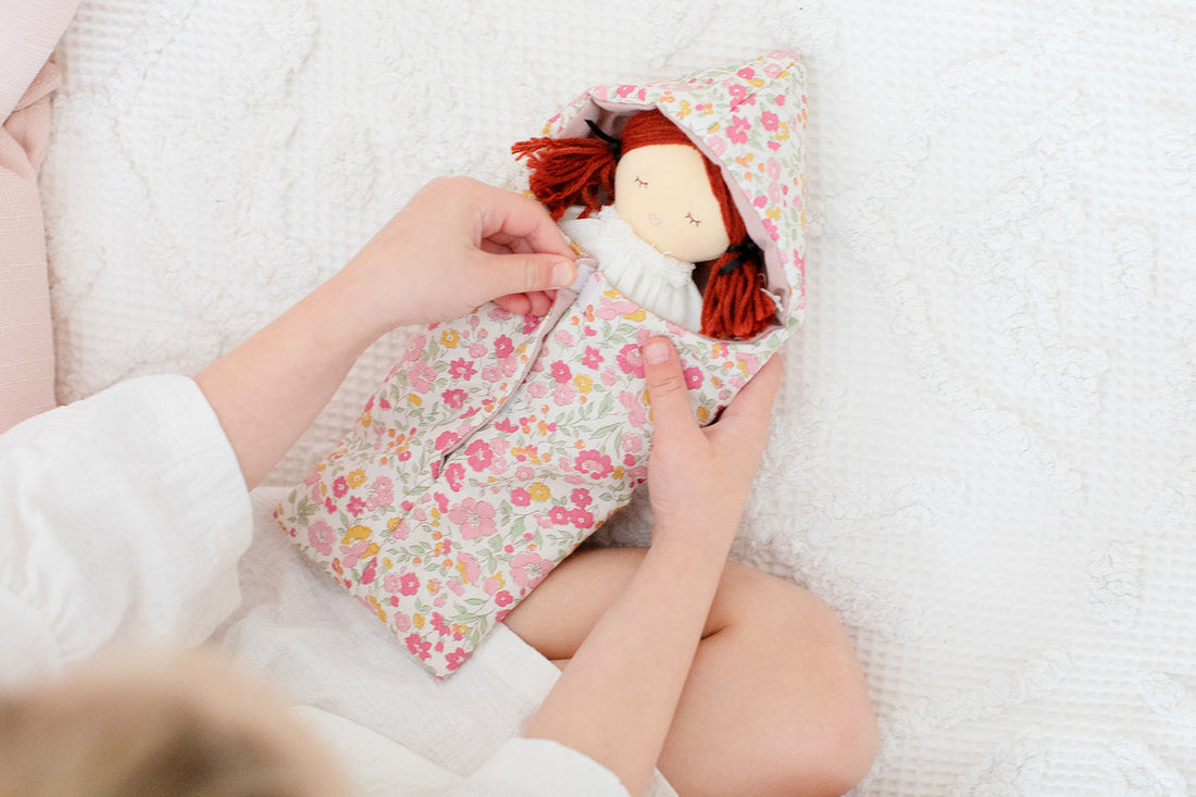 Child with doll in floral sleeping bag.