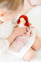 A child sits with a fabric doll in a floral carrier.