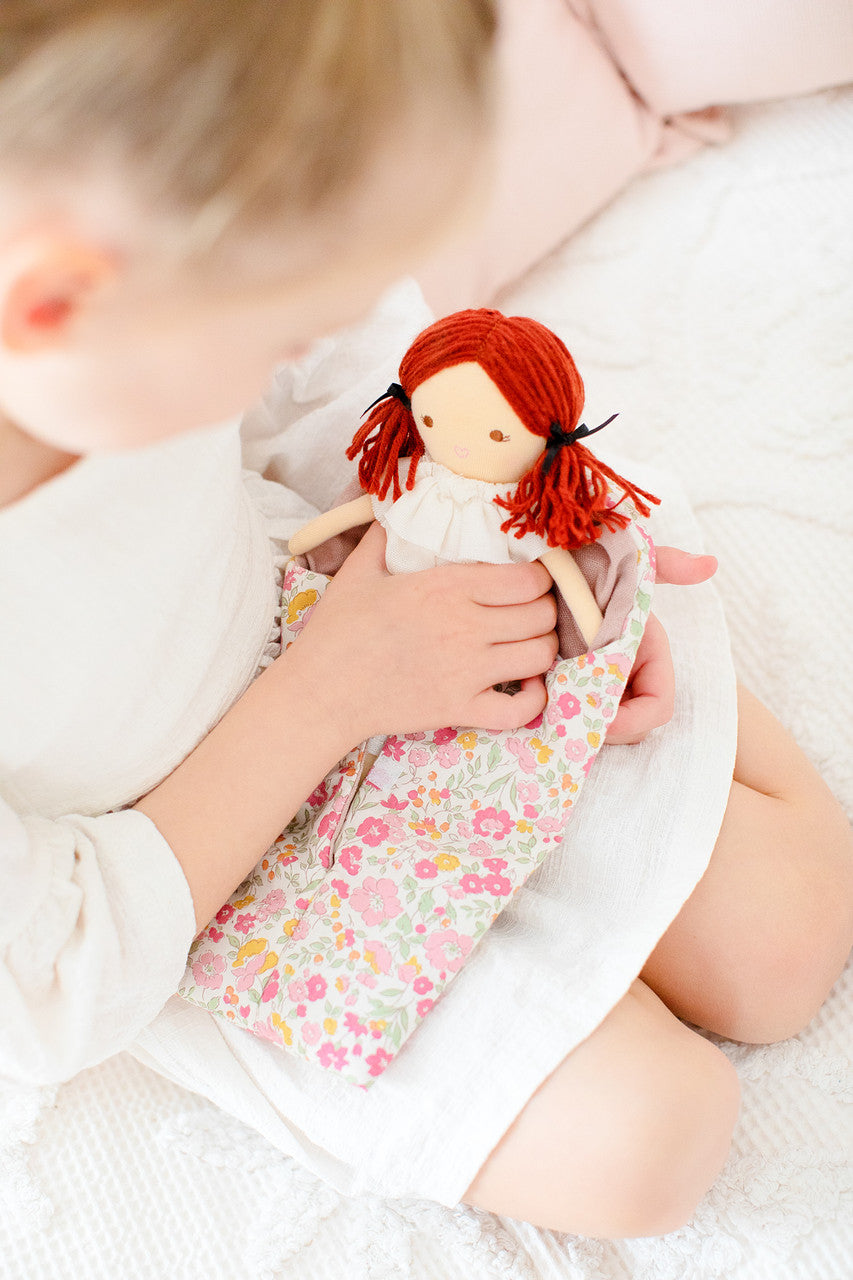 A child sits with a fabric doll in a floral carrier.