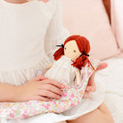 Girl holding rag doll with floral blanket.