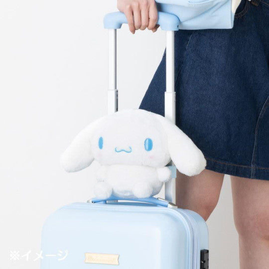 Person pulling a light blue suitcase with a white plush toy attached to the handle, wearing a denim skirt.