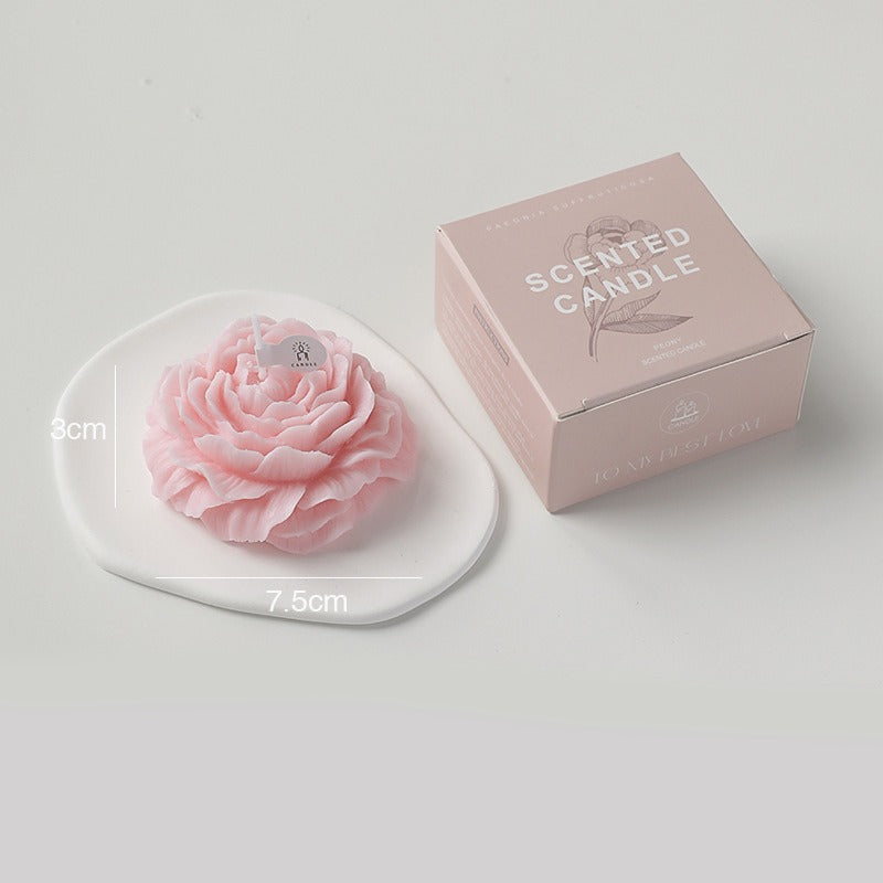 Pink peony scented candle by Jellycup on a white dish next to its box packaging.