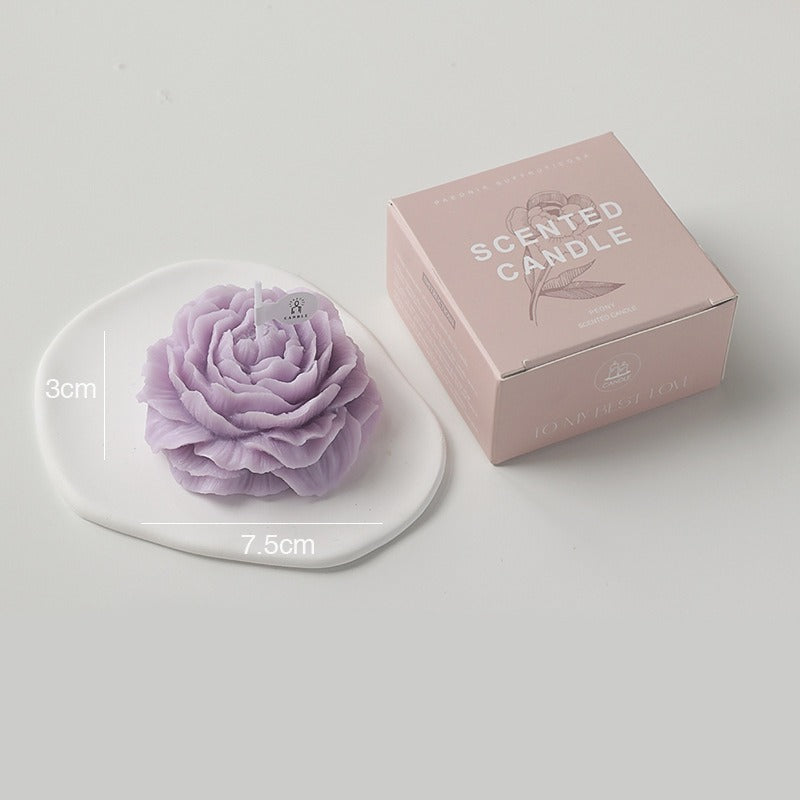 Purple peony candle by Jellycup on a white, irregular-shaped ceramic dish beside a pink box.