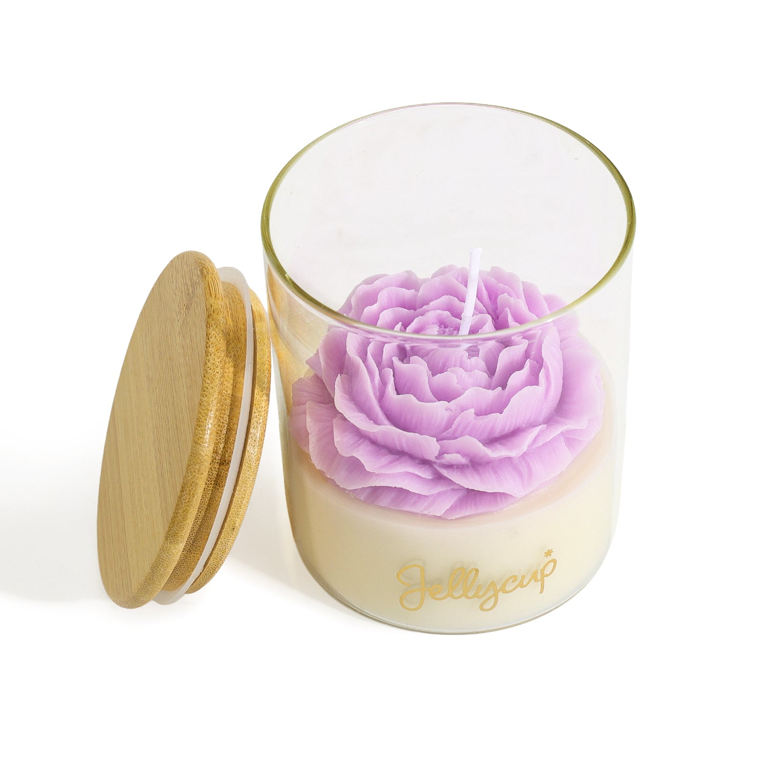 A clear glass jar candle with a light cream wax base, a large lavender-purple flower-shaped wax top, and a gold script logo reading 'Jellycup' on the front. A round bamboo-style lid with a gold rim leans against the jar on a clean white background.