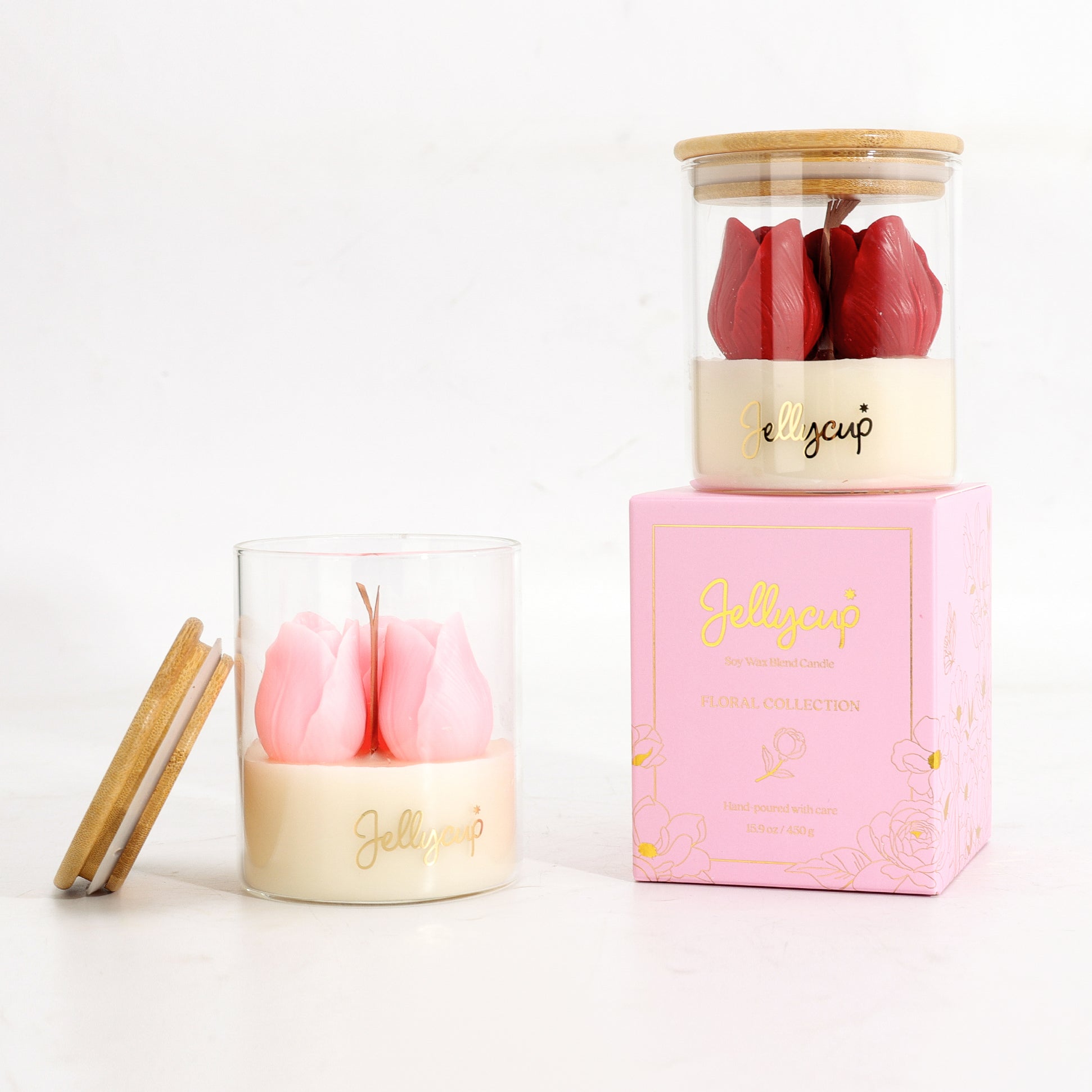 Two Jollycup scented candles in clear glass jars with bamboo lids, displayed alongside their pink branded box on a white background. One candle features pink tulip-shaped wax pieces, and the other features red tulip-shaped wax pieces.