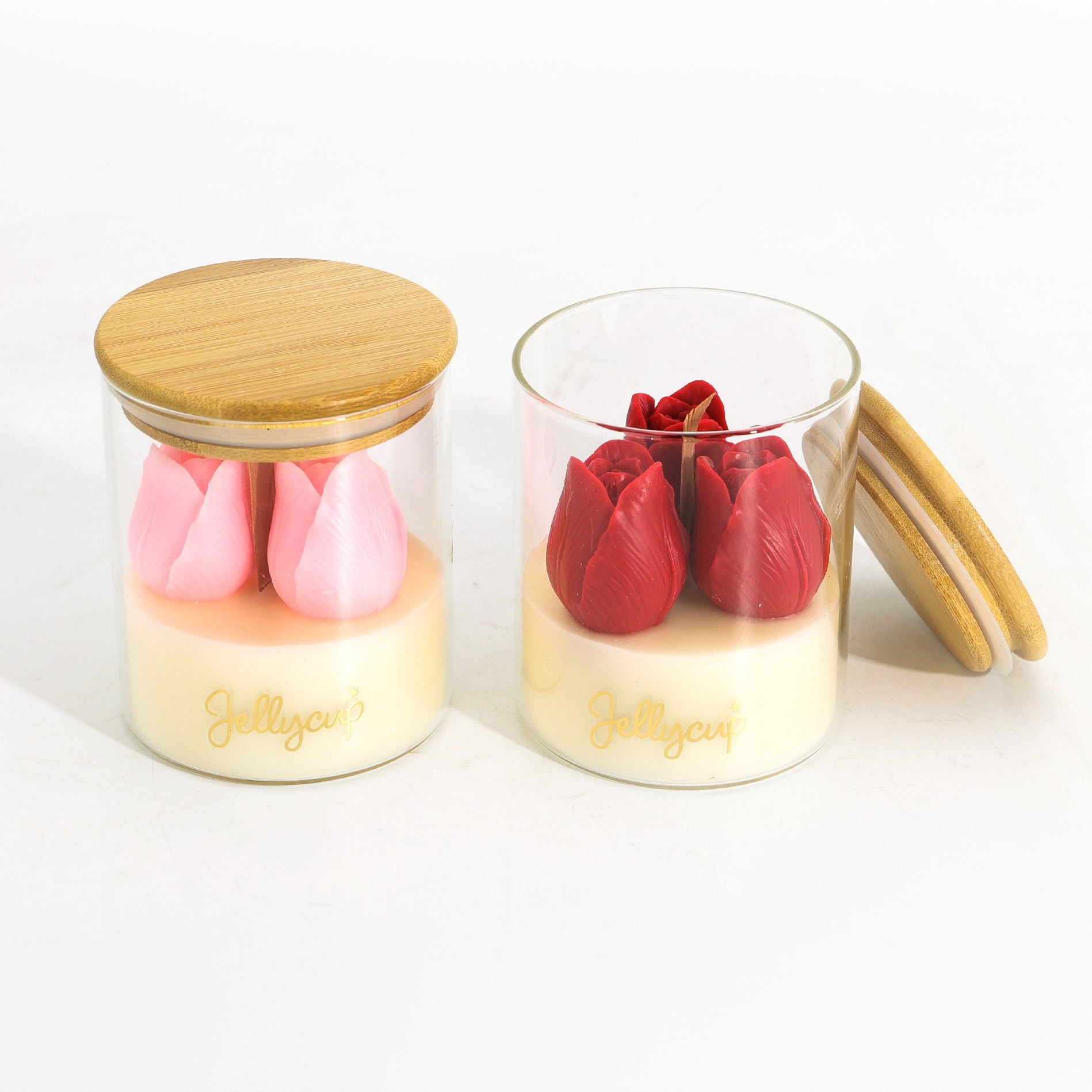 Two clear glass jars with bamboo lids on a white background, containing layered cream-colored wax with pink and red lotus flower shapes. One jar is closed, and the other is open with its lid leaning against it.