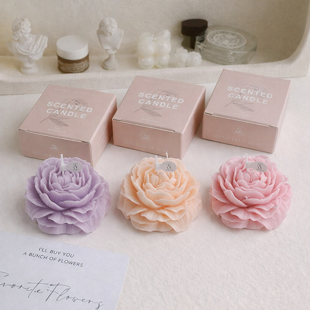 Flower-shaped scented candles by Jellycup, displayed in three colors, with decorative boxes on a textured surface.