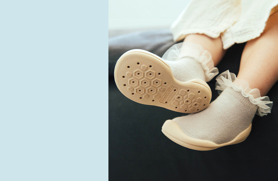 Close-up of a baby wearing Komuello shoes with flexible rubber soles and soft socks with frilly edges, designed for comfort and first steps.