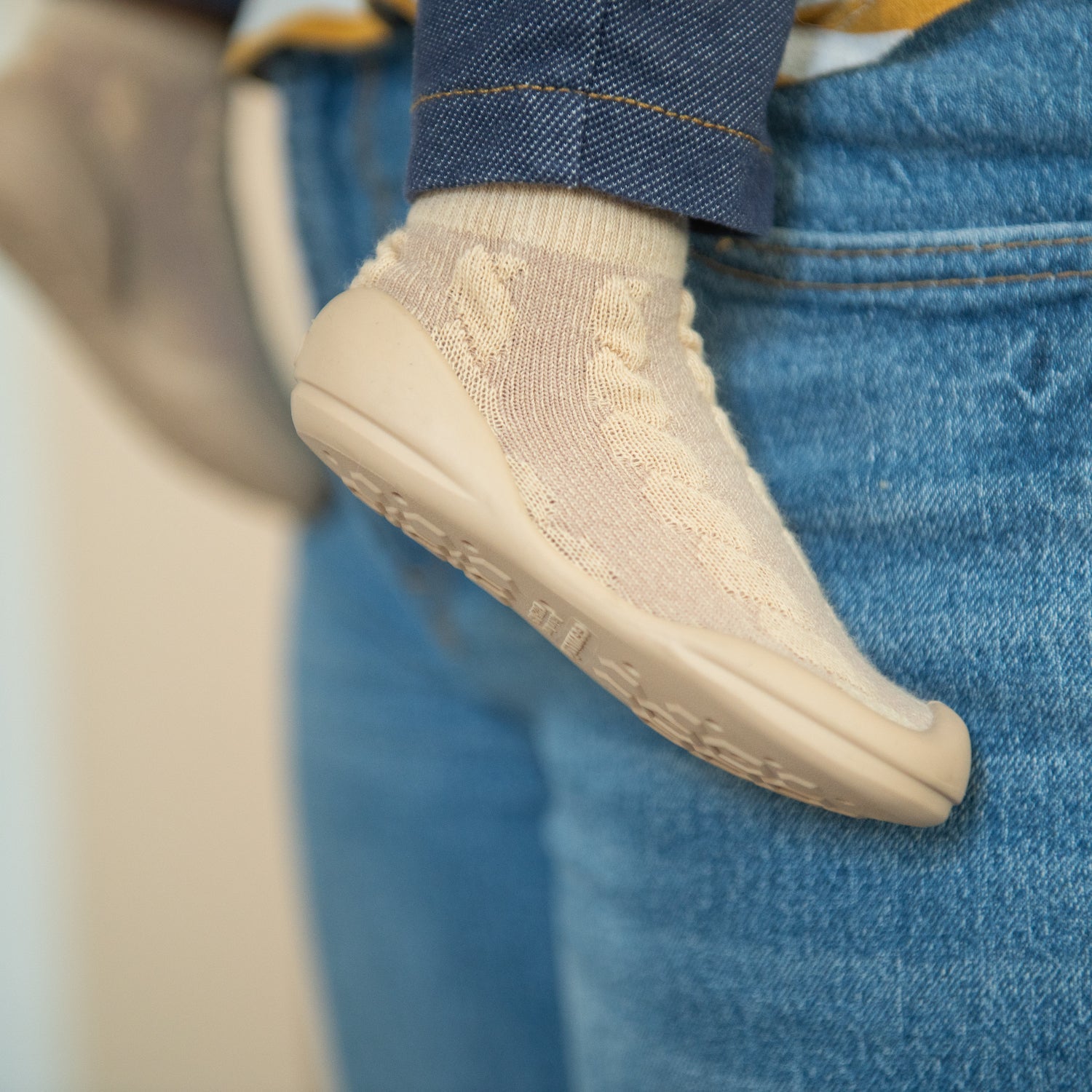 A baby wearing a tan sock-shoe and blue denim.