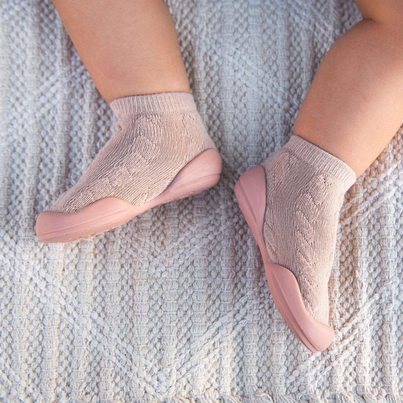 Close-up of baby's feet in peach-colored sock shoes on a white textured blanket.